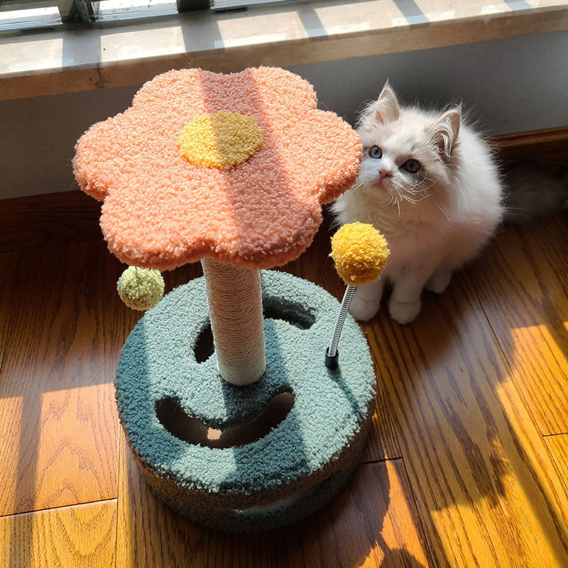 Cat scrambler with orange flower top and pom-poms next to white kitten on wooden floor cat scratch board
